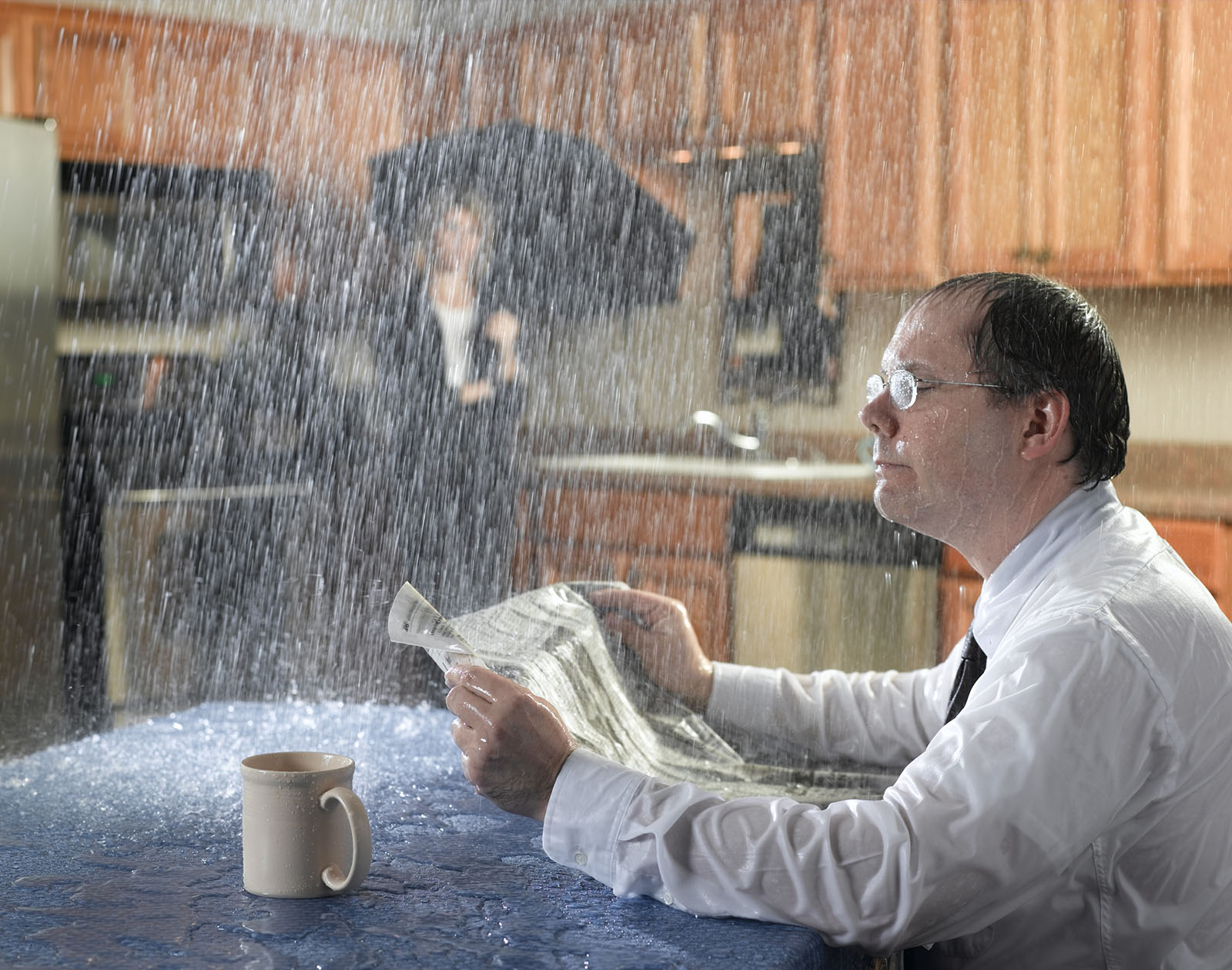 Man at kitchen table getting soaked from water leaks in roof